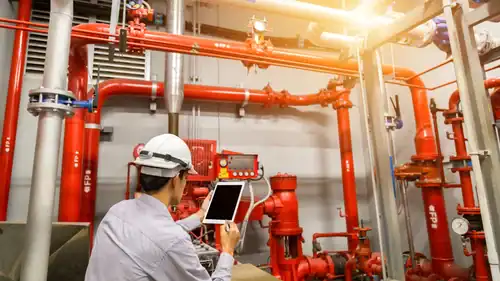 Engineer checking a tablet beside red fire sprinkler piping